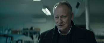 Movie still from “Out Stealing Horses” (2019), directed by Hans Petter Moland – An older man wearing a sweater and a scarf; Close Up shot, Over the shoulder angle