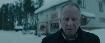 Movie still from “Out Stealing Horses” (2019), directed by Hans Petter Moland – An older man standing in front of a building; Close Up shot, Over the shoulder angle