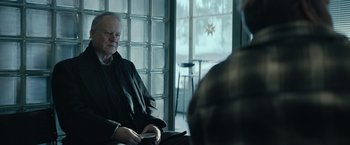 Movie still from “Out Stealing Horses” (2019), directed by Hans Petter Moland – An older man sitting on a chair in front of a window; Medium shot, Over the shoulder angle