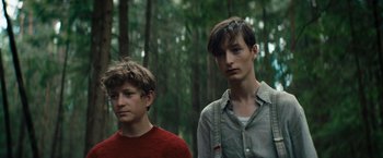 Movie still from “Out Stealing Horses” (2019), directed by Hans Petter Moland – Two young men standing next to each other in the woods; Close Up shot, Low angle