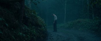 Movie still from “Out Stealing Horses” (2019), directed by Hans Petter Moland – A man standing in the middle of a road in the woods; Wide shot, Low angle