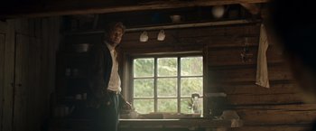 Movie still from “Out Stealing Horses” (2019), directed by Hans Petter Moland – A man standing in front of a window in a room; Medium shot, Low angle
