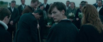 Movie still from “Out Stealing Horses” (2019), directed by Hans Petter Moland – A man in a crowd of people holding a stick; Close Up shot, Over the shoulder angle