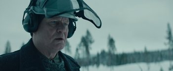 Movie still from “Out Stealing Horses” (2019), directed by Hans Petter Moland – An older man wearing a helmet and ear muffs; Close Up shot, Over the shoulder angle
