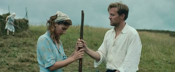 Movie still from “Out Stealing Horses” (2019), directed by Hans Petter Moland – A man and a woman holding a stick in a field; Medium shot, Low angle