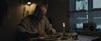 Movie still from “Out Stealing Horses” (2019), directed by Hans Petter Moland – An older man sitting at a dinner table with a lit candle; Medium shot, Over the shoulder angle