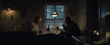 Movie still from “Out Stealing Horses” (2019), directed by Hans Petter Moland – Two men sitting at a dinner table eating dinner; Wide shot, High angle