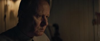 Movie still from “Out Stealing Horses” (2019), directed by Hans Petter Moland – An older man looking into the distance in a dimly - lit room; Close Up shot, Over the shoulder angle