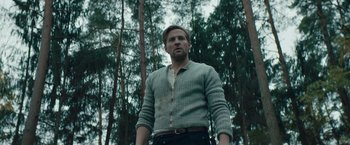Movie still from “Out Stealing Horses” (2019), directed by Hans Petter Moland – A man standing in a wooded area with trees in the background; Medium shot, Low angle