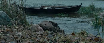 Movie still from “Out Stealing Horses” (2019), directed by Hans Petter Moland – A man laying on the ground near a body of water; Medium shot, High angle