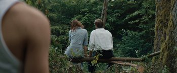 Movie still from “Out Stealing Horses” (2019), directed by Hans Petter Moland – A man and a woman sitting on top of a log; Wide shot, High angle