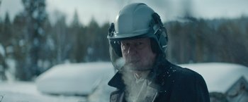 Movie still from “Out Stealing Horses” (2019), directed by Hans Petter Moland – An older man wearing a hard hat in the snow; Close Up shot, Over the shoulder angle
