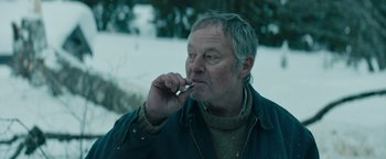 Movie still from “Out Stealing Horses” (2019), directed by Hans Petter Moland – An older man is smoking a cigarette in the snow; Close Up shot, Low angle