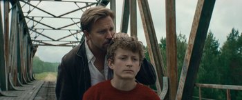 Movie still from “Out Stealing Horses” (2019), directed by Hans Petter Moland – A man standing next to a young boy on top of a bridge; Close Up shot, Over the shoulder angle