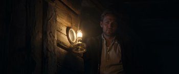 Movie still from “Out Stealing Horses” (2019), directed by Hans Petter Moland – A man standing next to a light in a room; Medium shot, Low angle