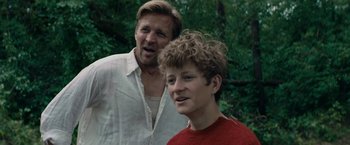 Movie still from “Out Stealing Horses” (2019), directed by Hans Petter Moland – A man standing next to a young boy in the woods; Close Up shot, Over the shoulder angle