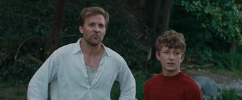 Movie still from “Out Stealing Horses” (2019), directed by Hans Petter Moland – A man standing next to a boy in a red shirt; Medium shot, Low angle