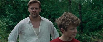 Movie still from “Out Stealing Horses” (2019), directed by Hans Petter Moland – A man standing next to a boy in a red shirt; Medium shot, Low angle