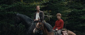 Movie still from “Out Stealing Horses” (2019), directed by Hans Petter Moland – Two men riding on the back of a brown horse; Medium shot, Low angle