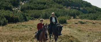 Movie still from “Out Stealing Horses” (2019), directed by Hans Petter Moland – A man and a woman riding horses through a field; Wide shot, Low angle