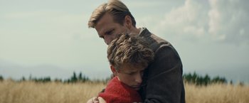 Movie still from “Out Stealing Horses” (2019), directed by Hans Petter Moland – A man and a boy are hugging in a field; Close Up shot, Over the shoulder angle