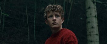 Movie still from “Out Stealing Horses” (2019), directed by Hans Petter Moland – A young man in a red sweater is looking at the camera; Close Up shot, Low angle