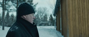 Movie still from “Out Stealing Horses” (2019), directed by Hans Petter Moland – A man standing in front of a building in the snow; Close Up shot, Over the shoulder angle