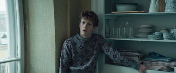 Movie still from “Out Stealing Horses” (2019), directed by Hans Petter Moland – A young man leaning against a wall in front of a shelf; Close Up shot, High angle