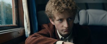 Movie still from “Out Stealing Horses” (2019), directed by Hans Petter Moland – A young man with curly blonde hair wearing a brown jacket; Close Up shot, High angle