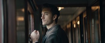 Movie still from “Out Stealing Horses” (2019), directed by Hans Petter Moland – A young man standing next to a train window; Close Up shot, Over the shoulder angle