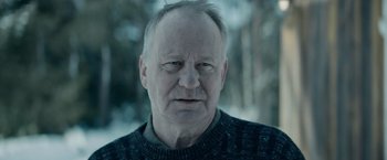 Movie still from “Out Stealing Horses” (2019), directed by Hans Petter Moland – An older man with a gray beard and a sweater; Close Up shot, Over the shoulder angle