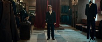 Movie still from “Out Stealing Horses” (2019), directed by Hans Petter Moland – A man in a suit standing in a room with red drapes; Wide shot, Low angle
