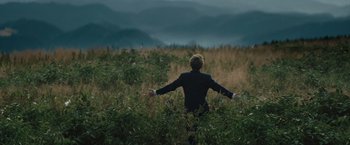 Movie still from “Out Stealing Horses” (2019), directed by Hans Petter Moland – A man standing in a field with his arms outstretched; Extreme Wide shot, Low angle