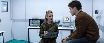 Movie still from “The 5th Wave” (2016), directed by J Blakeson – A woman in a military fatigues is talking to a man in a lab; Medium shot, Over the shoulder angle