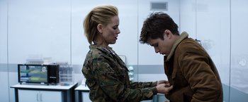 Movie still from “The 5th Wave” (2016), directed by J Blakeson – A woman in a military uniform is helping a young man; Medium shot, Over the shoulder angle