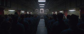 Movie still from “The 5th Wave” (2016), directed by J Blakeson – A group of people sitting in front of a man in a room; Extreme Wide shot, Over the shoulder angle