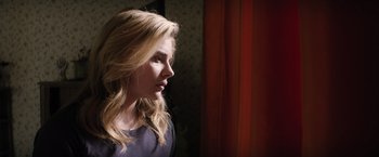 Movie still from “The 5th Wave” (2016), directed by J Blakeson – A woman standing in front of a red curtain looking out a window; Close Up shot, Low angle