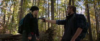 Movie still from “The 5th Wave” (2016), directed by J Blakeson – A man pointing a gun at a woman in the woods; Medium shot, Over the shoulder angle