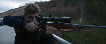 Movie still from “The 5th Wave” (2016), directed by J Blakeson – A man is holding a rifle and looking through the scope; Medium shot, Over the shoulder angle