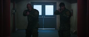Movie still from “The 5th Wave” (2016), directed by J Blakeson – Two men in uniform are holding guns in a dark room; Medium shot, Over the shoulder angle