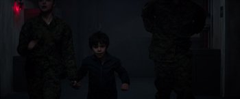Movie still from “The 5th Wave” (2016), directed by J Blakeson – A young boy standing next to a group of trees; Medium shot, High angle