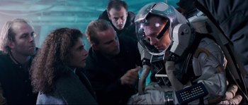 Movie still from “The Abyss” (1989), directed by James Cameron – A group of people standing around a man in a space suit; Medium shot, High angle
