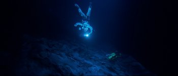 Movie still from “The Abyss” (1989), directed by James Cameron – A man is diving in the ocean with a light; Wide shot, Overhead angle