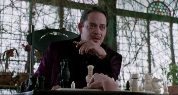 Movie still from “The Addams Family” (1991), directed by Barry Sonnenfeld – A man sitting in front of a chess board holding a cigar; Close Up shot, Over the shoulder angle
