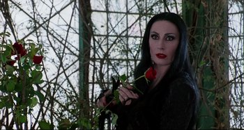 Movie still from “The Addams Family” (1991), directed by Barry Sonnenfeld – A woman holding a red rose while wearing a black outfit; Close Up shot, Over the shoulder angle