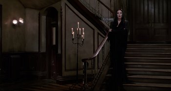 Movie still from “The Addams Family” (1991), directed by Barry Sonnenfeld – A woman standing on the stairs of a house; Wide shot, Low angle