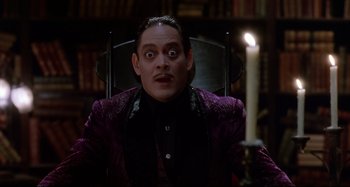 Movie still from “The Addams Family” (1991), directed by Barry Sonnenfeld – A man sitting in a chair in front of a lit candle; Close Up shot, Low angle