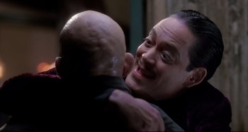 Movie still from “The Addams Family” (1991), directed by Barry Sonnenfeld – A man hugging a bald man in a dark room; Close Up shot, Over the shoulder angle