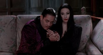 Movie still from “The Addams Family” (1991), directed by Barry Sonnenfeld – A man and a woman sitting on top of a couch; Medium shot, High angle