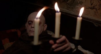 Movie still from “The Addams Family” (1991), directed by Barry Sonnenfeld – A man with bald head holding two lit candles in front of his face; Close Up shot, High angle